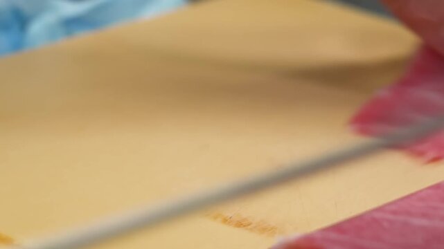 Close-up shot of a professional sushi chef's hands using a traditional Japanese knife to slice a fresh saku block of fatty Bluefin tuna (Otoro). The footage highlights the delicate texture, rich marbl