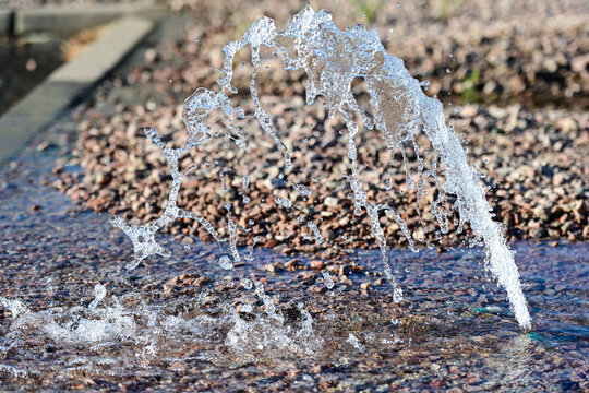 Malfunctioning landscape sprinkler head discharging water onto decorative gravel surface, representing water leakage, system inefficiency, and landscape maintenance needs
