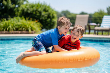 Fototapeta premium Two young boys playing on an orange tube in a pool