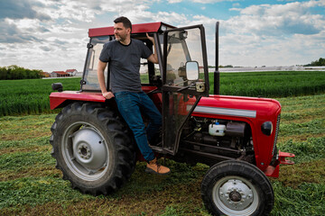 Obraz premium Handsome man sitting on the tractor and looking across the field, wheat in the background, agricultural farm