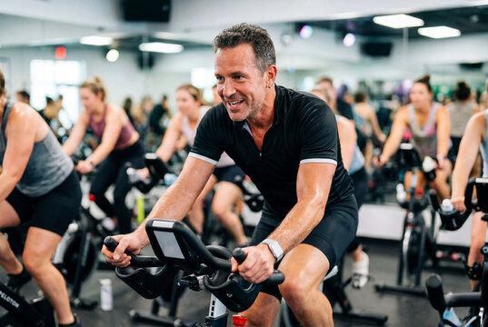Middle aged man sweating while intensely riding stationary bike in spin class