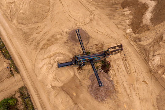 Aerial view of an industrial conveyor belt machine sorting sand and gravel in a quarry with tire tracks on the ground in Nemencine, Vilnius County, Lithuania.