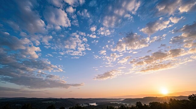 Vast landscape at sunrise with glowing sun and soft clouds over rolling hills.