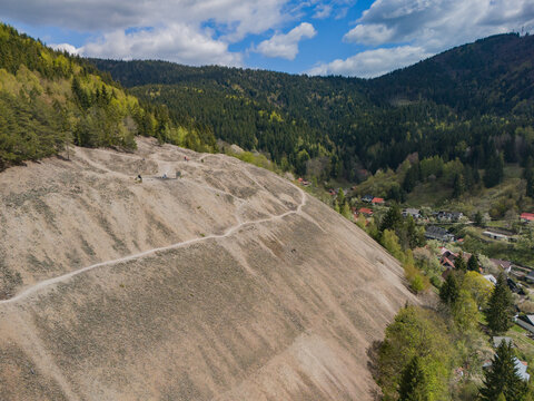 Aerial view of the historic mining mound and village surrounded by dense green forests and rolling hills under a cloudy sky Spania Dolina, Banska Bystrica Region, Slovakia.