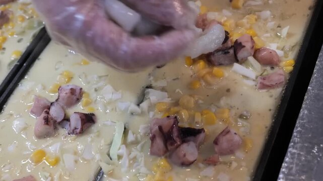 close-up, top-down shot of a large flat cooking tray filled with a creamy yellow base, topped with sweet corn kernels, diced ham, and pieces of seafood. This footage illustrates the meticulous prepara