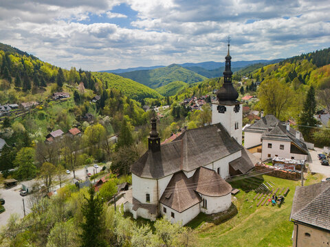 Aerial view of the historic Church of the Conversion of the Lord surrounded by traditional houses and lush green hills Spania Dolina, Banska Bystrica Regio, Slovakia.