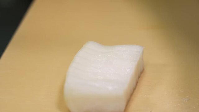 Close-up of a chef's hands using a sharp Japanese kitchen knife to slice a large, white daikon radish into uniform rectangular blocks. The footage highlights culinary precision and fresh vegetable pre