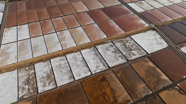 Aerial view of geometric salt evaporation ponds with varying shades of pink and brown in Cagliari, Sardinia, Italy.