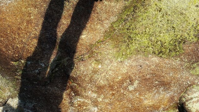 Silhouette shadow of a person cast on textured rock surface with natural sunlight, creating dramatic contrast and artistic composition