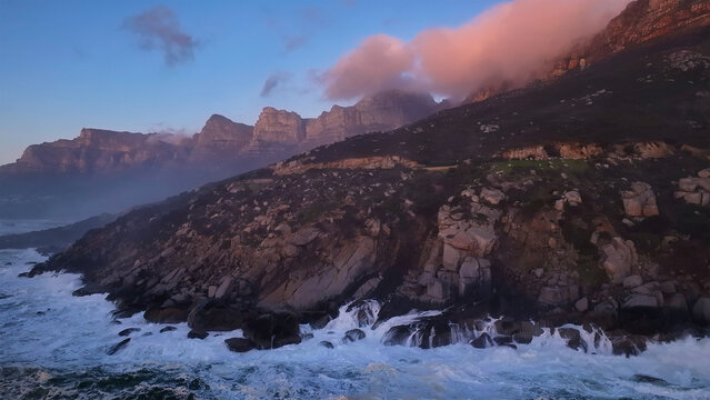 Aerial view of the Twelve Apostles mountain range with crashing waves against rocky cliffs under a sunset sky Cape Town, Western Cape, South Africa.