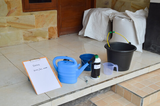 Top-down quarter-left angle view of a garden fertilization setup. Features a 10ml dose instruction for Bio NPK mixture with 5L of water in a black bucket for soil feeding.