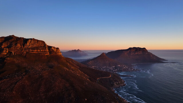 Aerial view of the rugged peaks of Table Mountain and Lion's Head overlooking the Atlantic coastline during a golden sunset in Cape Town, Western Cape, South Africa.