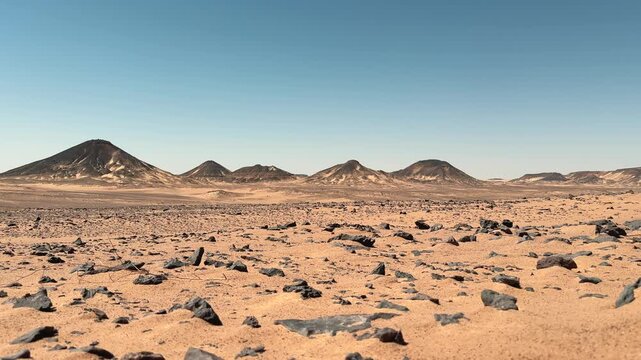 Low angle slider motion of volcanic desert plain covered with black basalt stones under clear sky