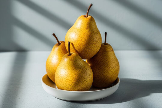 Four yellow pears stacked on a white plate with dramatic sunlight shadows on light blue background, minimal fruit photography