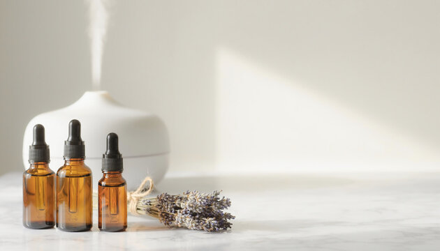 Aromatherapy set featuring amber dropper bottles and dried lavender on a marble surface for mental health and relaxation. White electric oil diffuser emitting mist in a bright room.