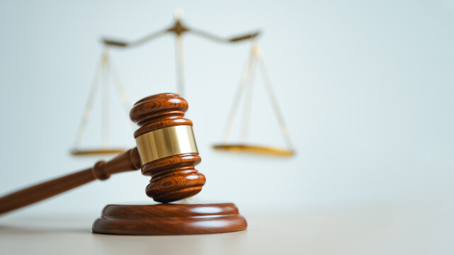 Wooden judge gavel with justice scales in background, symbolizing legal authority, court decisions, fairness, law enforcement and professional judicial system concepts.