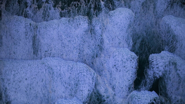 Aerial view of powerful ocean waves crashing with white foam and spray creating abstract textures on the deep blue water Cape Town, Western Cape, South Africa.