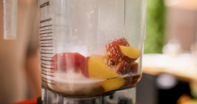 Electric blender. Making fruit drink. Fresh peaches pieces in professional automatic machine with alcohol water syrup in restaurant.