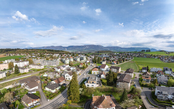 Aerial view of residential houses, green meadows, and the Jura mountains under a blue sky in Biberist, Solothurn, Switzerland.