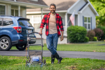 Fototapeta premium Lawnmower mow the green grass. Man gardener cut the grass. Garden care. Electric lawn mower. Landscaping. Landscape design. Backyard grass maintenance. Hispanic gardener. Mowing day outdoors