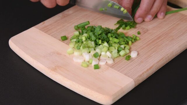 person using kitchen knife chopping fresh spring onion on wooden cutting board
