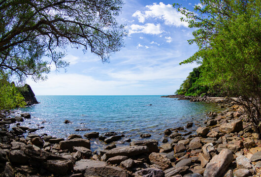 Scenic rocky beach at Koh Chang island with turquoise sea water and lush green trees under a bright blue sky, Thailand