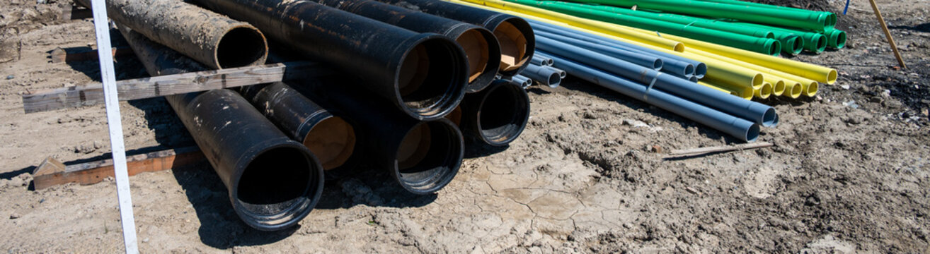 Stacks of sewar and water pipes, and electrical and telecommunication conduit, new residential development construction project in earthworks stage installing underground utilities
