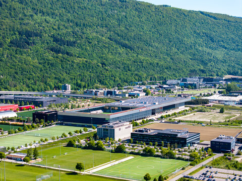 Aerial view of the Biel Bienne Boezingenfeld Champ industrial area featuring modern commercial buildings and sports fields near a lush forested mountain in Biel Bienne, Canton of Bern, Switzerland.