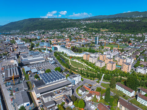 Aerial view of the modern architecture of the Swatch headquarters, industrial zones, and residential areas surrounded by green parks and hills in Biel Bienne, Canton of Bern, Switzerland.