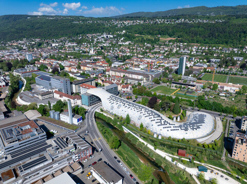 Aerial view of the Swatch and Omega Campus featuring the iconic curved timber structure spanning over the Suze river and a road in Biel Bienne, Canton of Bern, Switzerland.