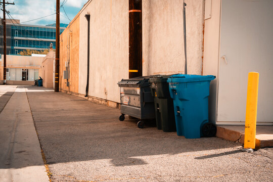Urban alleyway with dumpsters and a bright blue trash bin