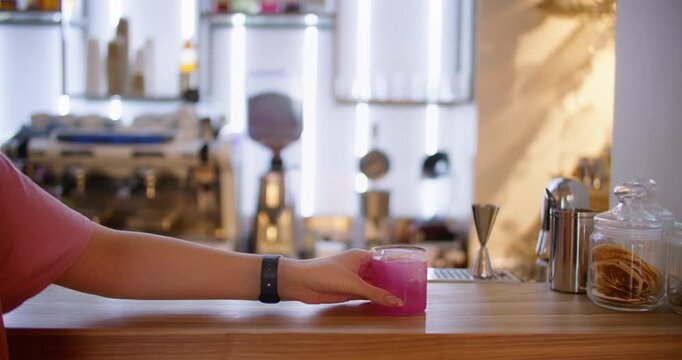 Cocktail bar. Taking beverage. Female customer hand reaching bright pink cold alcohol drink at pub counter in restaurant interior.