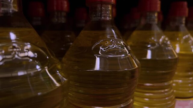 Close view of plastic bottles filled with cooking oil arranged in rows, golden liquid inside containers, retail or storage setting with repeated pattern