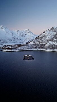 Vertical drone arc at polar night of cod farm in Ringvassoya and snowy landscape