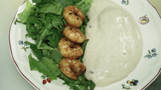 Plating food. Restaurant dish. Gloved chef hand serving frying shrimp with fresh greens creamy white sauce. Preparing healthy appetizer.
