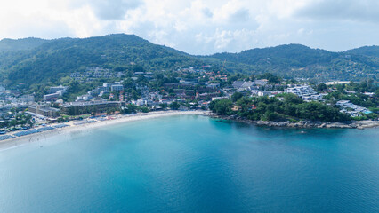 Obraz premium A coastal town nestled between green hills with a sandy beach meeting calm blue waters under a partly cloudy sky.