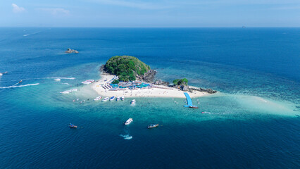 Aerial view of a small lush island surrounded by turquoise and deep blue ocean water, with boats anchored nearby and people enjoying the beach. © PIPAT