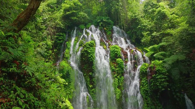 Tropical waterfall of many cascading streams flowing through lush greenery. Banyu Wana Amertha, Bali