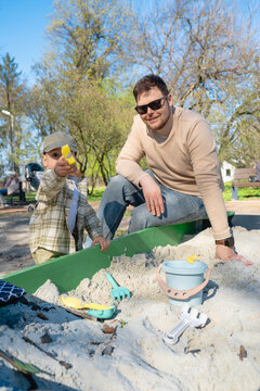 Father and son playing in sandbox outdoors on sunny day.
