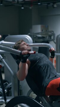 Muscular Caucasian bodybuilder performs machine incline chest press targeting upper pectoral muscles on incline bench in modern gym - verical