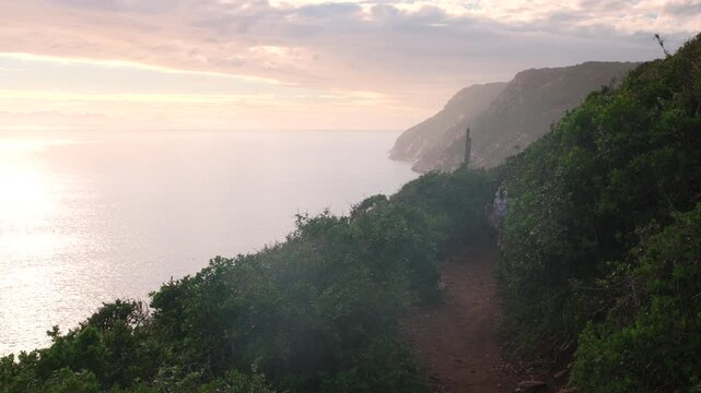 Hikers on scenic Robberg Hiking Trail in Plettenberg Bay with vibrant clouds and light mist at sunrise