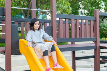 Excited Asian girl sliding quickly down a bright yellow playground slide, shouting with joy and adrenaline © Kwangmoozaa