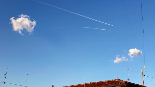Two aircraft leave contrails across a clear blue sky with clouds