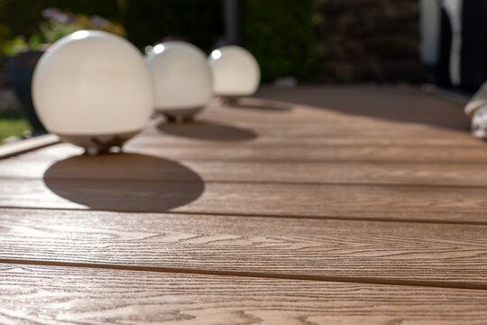 Modern spherical lamps on WPC decking with strong shadows. Outdoor design, premium material and summer evening atmosphere.