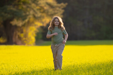 Naklejka premium Child running in summer field. Happy kid run outdoors. Child on nature. Child in run motion on grass. Kid running at sun light. Teen running in meadow. Portrait of running child.