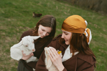 Naklejka premium Cheerful women outdoors, two friends share a gentle moment with a small goat, kid, soft light, warm colors, grassy field, relaxed interaction, candid lifestyle scene, affectionate dozen smiles