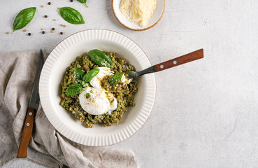 Top view of Buckwheat porridge with spinach pesto and poached eggs and fork inside served on light table. © Taborisova