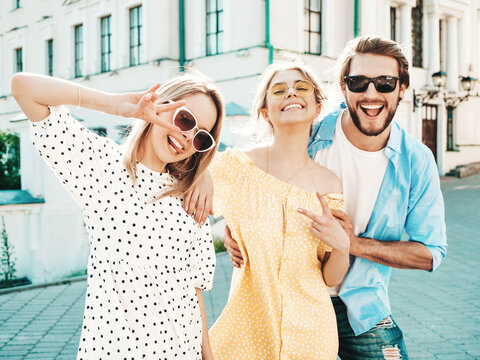 Group of young three stylish friends posing in the street. Fashion man and two cute dressed in casual summer clothes. Smiling models having fun in sunglasses.Cheerful women and guy at susnet