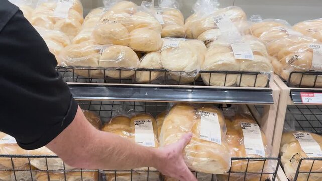 A male hand reaching for a packaged loaf of fresh white bread from a supermarket shelf, a close-up cinematic shot.