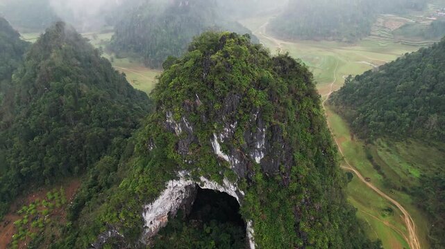 Forested karst hills in Northern Vietnam covered by dense fog with low visibility creating moody atmospheric landscape in soft diffused light aerial drone view